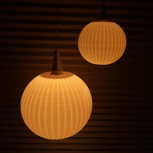 May include: Two spherical pendant lights with a ribbed design, hanging from the ceiling. The lights are a warm, off-white color, and the background is a dark brown with horizontal lines.