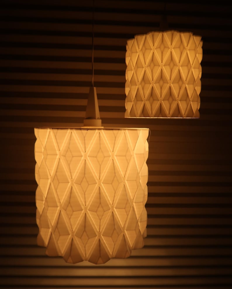May include: Two geometric pendant lights with a warm glow. The lampshades have a repeating diamond pattern, creating a textured surface. The lights hang from the ceiling against a backdrop of horizontal lines.