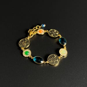 Peut inclure: Bracelet doré orné de pierres précieuses colorées et d'éléments circulaires décoratifs. Le bracelet comprend des pierres ovales et circulaires bleues, vertes, oranges et jaunes, rehaussées de petits cristaux transparents.