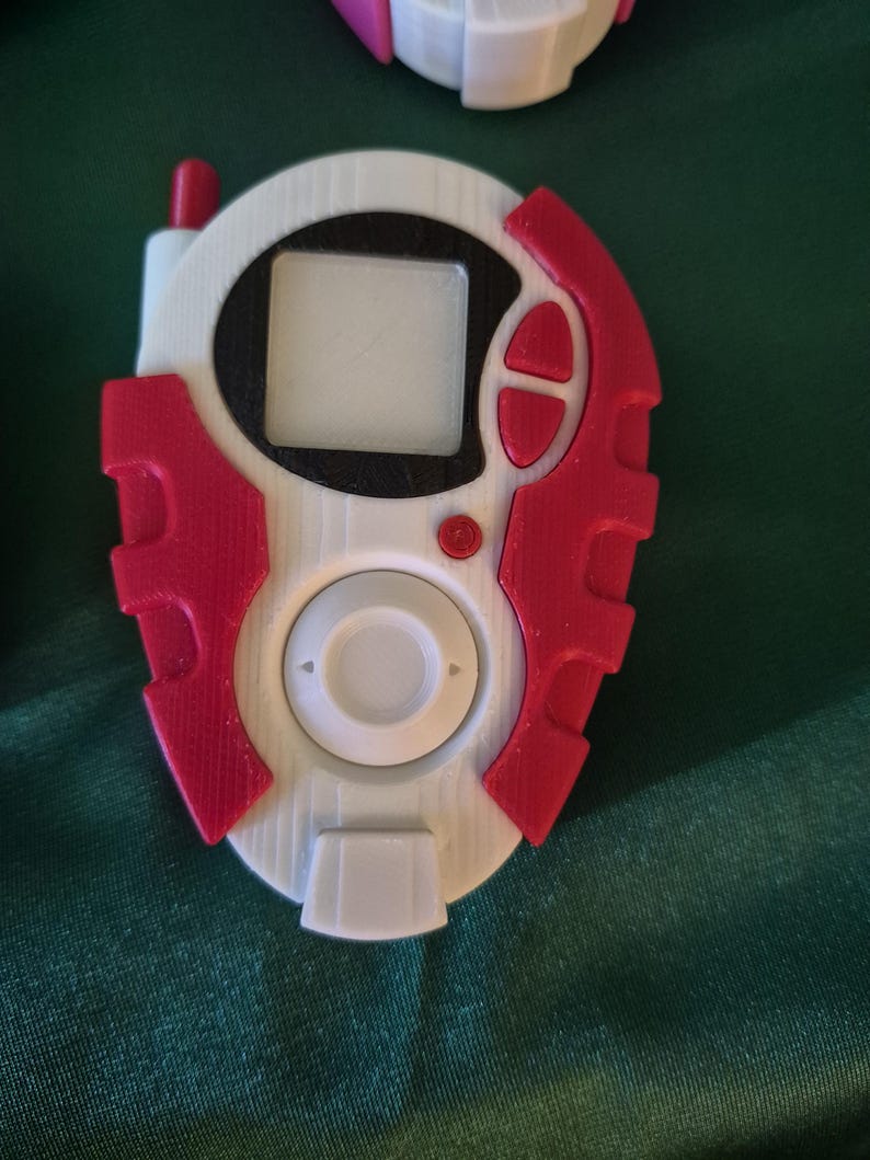 May include: A white and red handheld device with a small screen and buttons. The device has a circular centre with a rectangular screen and a red antenna. The device is likely a toy or collectible item.