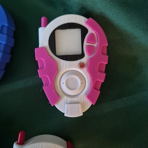 May include: A white and pink handheld device with a screen, buttons, and antenna. The device has a circular centre with a white button and a rectangular screen. The pink accents include buttons and side panels. Other devices are visible.