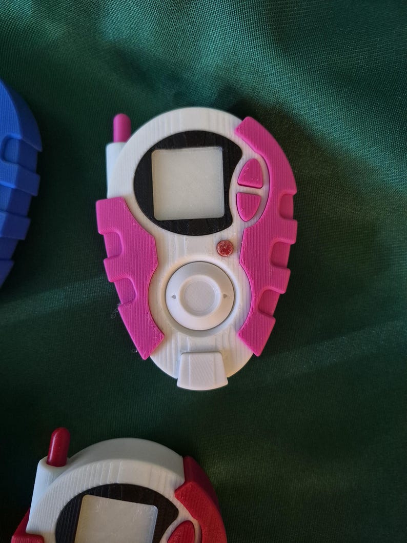 May include: A white and pink handheld device with a screen, buttons, and antenna. The device has a circular centre with a white button and a rectangular screen. The pink accents include buttons and side panels. Other devices are visible.