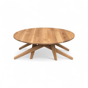 May include: A round wooden coffee table with a natural finish. The table has a circular top and a unique base design with angled legs. The table is made of light-colored wood and is suitable for a living room or lounge area.