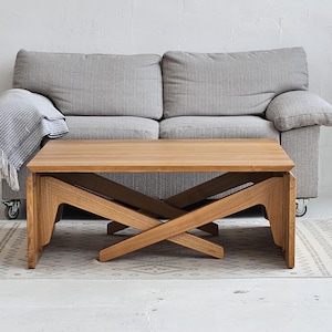 May include: A rectangular coffee table made of light brown wood featuring a flat top surface and a base constructed with two intersecting, angled support legs that form an X-shape on each side, providing a stable foundation for the furniture piece.