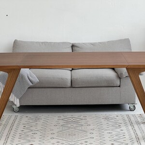 K&ouml;nnte beinhalten: Ein rechteckiger Esstisch aus Holz mit glatter, mittelbrauner Oberfl&auml;che und angewinkelten, konisch zulaufenden Beinen. Der Tisch hat eine saubere, flache Oberfl&auml;che mit sichtbarer Holzmaserung und eine stabile Konstruktion.