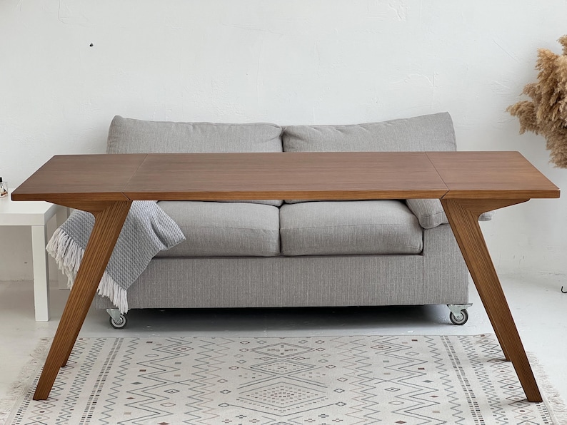 K&ouml;nnte beinhalten: Ein rechteckiger Esstisch aus Holz mit glatter, mittelbrauner Oberfl&auml;che und angewinkelten, konisch zulaufenden Beinen. Der Tisch hat eine saubere, flache Oberfl&auml;che mit sichtbarer Holzmaserung und eine stabile Konstruktion.