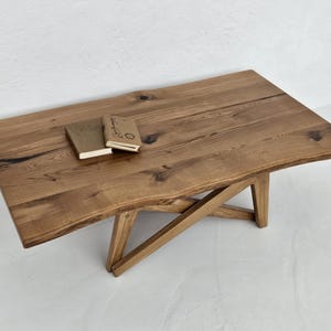 May include: A rectangular wooden coffee table with a natural finish. The table has a live edge on one side and two small books on top. The legs are angled and cross each other for support. The table is approximately 152 cm long.