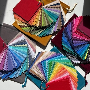 May include: Four sets of fabric swatches arranged in a fan shape, each attached to a metal ring and resting on a matching velvet drawstring pouch. The swatches feature a wide spectrum of colours including red, orange, yellow, green, blue, and purple.