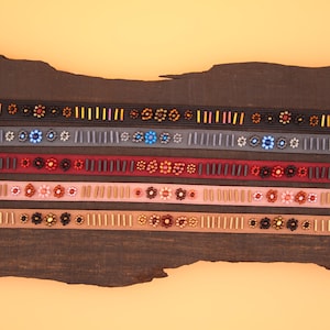 May include: A collection of six beaded trims with different colors and patterns, including black, red, pink, and brown. The trims are arranged on a wooden surface.