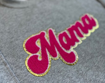 May include: A gray sweatshirt with a pink and gold "Mama" appliqué.