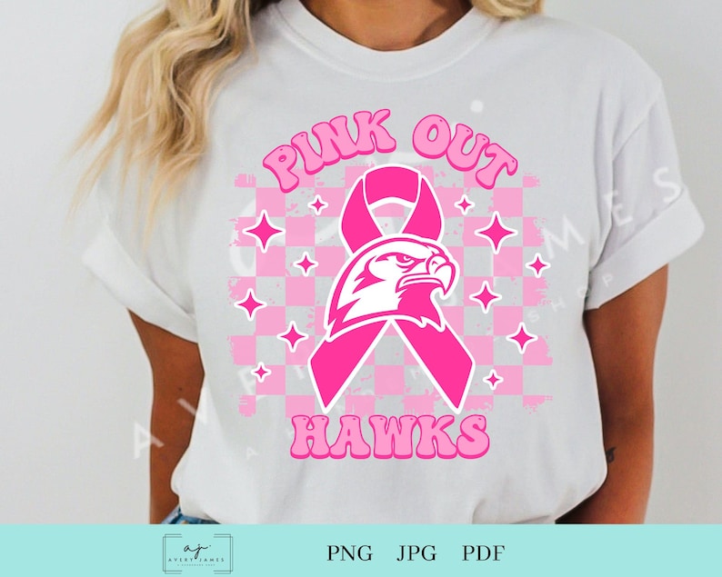 Op de afbeelding: Pink Out Hawks T-shirt ontwerp met een roze lint en een witte adelaar mascotte. Het ontwerp heeft een geruite achtergrond met roze sterren.