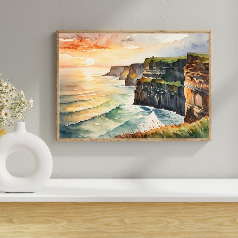 May include: Watercolor painting of a coastal landscape featuring cliffs and ocean waves under a sunset sky. The artwork is framed in a light brown wooden frame. The color palette includes shades of orange, blue, green, and brown.