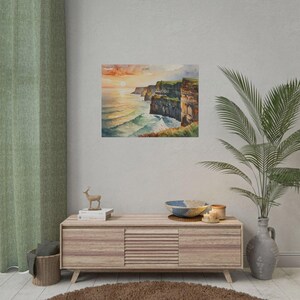 May include: Watercolor print of a coastal landscape featuring cliffs, ocean waves, and a sunset. The artwork is displayed on a wall, with a wooden cabinet and decorative items in the foreground. The color palette includes shades of orange, blue, and green.
