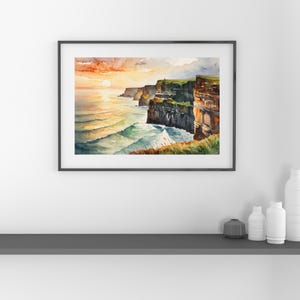 May include: Watercolor painting of a coastal landscape featuring cliffs and ocean waves under a sunset sky. The artwork is framed in a black frame and depicts a vibrant scene with shades of orange, blue, and green.