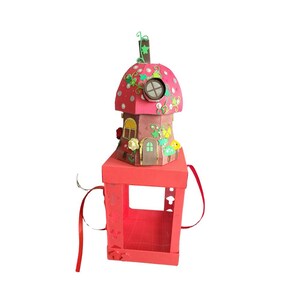 Puede incluir: Una casa de color rojo y marrón con forma de hongo, con una ventana y enredaderas verdes. La casa está sentada sobre una caja roja con una manija y una ventana. La caja tiene una cinta roja atada.