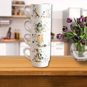 May include: A stack of four white ceramic mugs with floral and teacup designs. The mugs are stacked on a wooden surface.