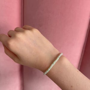 Pu&ograve; includere: Un braccialetto delicato fatto di piccole perline bianche e verdi. Il braccialetto &egrave; indossato al polso.