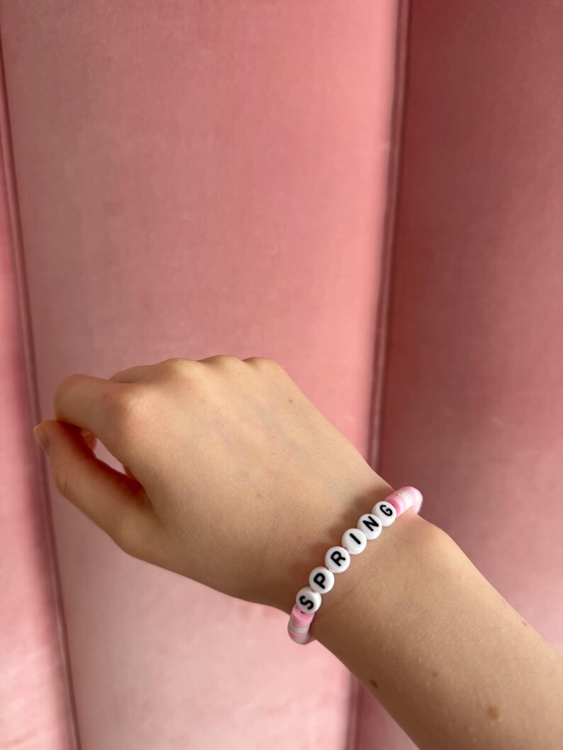 Pu&ograve; includere: Un braccialetto di perline rosa e bianche con la parola "SPRING" scritta in lettere nere.