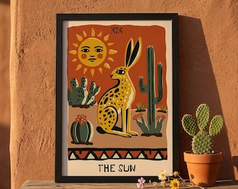 May include: Framed art print featuring a yellow and black spotted jackrabbit, cacti, and a smiling sun against an orange background. The text "THE SUN" is at the bottom. The artwork is in a black frame.