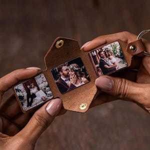 May include: A brown leather keychain with three small photo inserts. Each insert displays a different wedding photo. The keychain is held open, revealing the photos, and has a gold-colored metal ring.