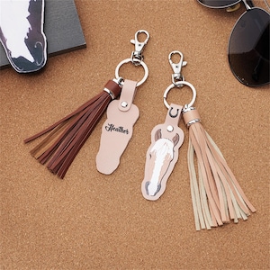 May include: Two leather keyrings with silver-tone clasps and tassels. One keyring features a horse head design, the other has the name "Heather" printed on it. The keyrings are light pink and brown.