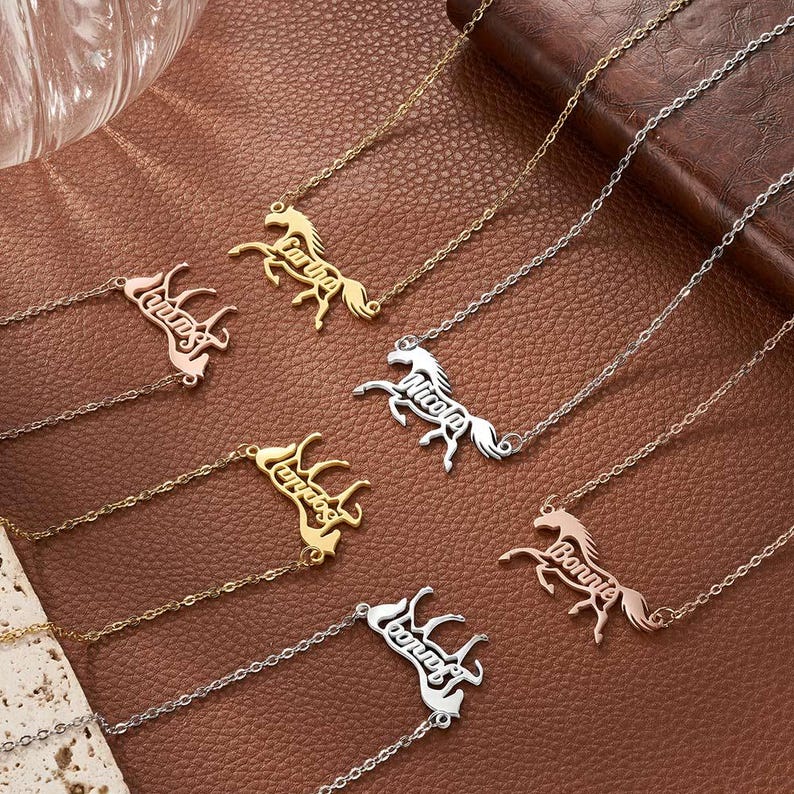 May include: A collection of six metal necklaces featuring horse-shaped pendants. Each pendant incorporates a name written in cursive script, including the names Cartha, Nicola, Sophia, and Bonnie. The necklaces are available in gold, silver, and rose gold tones.