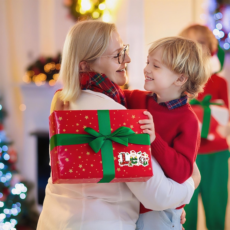 May include: A red gift box with gold stars and a green ribbon is held by a person. The box has a sticker that says "Leo" with Christmas-themed illustrations. The scene is festive, with a woman and child embracing, suggesting a holiday celebration.