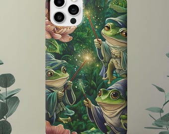 May include: A phone case featuring a whimsical illustration of green frog wizards in blue robes and pointed hats, holding wands with sparkling effects. The background includes pink flowers and lush green foliage.