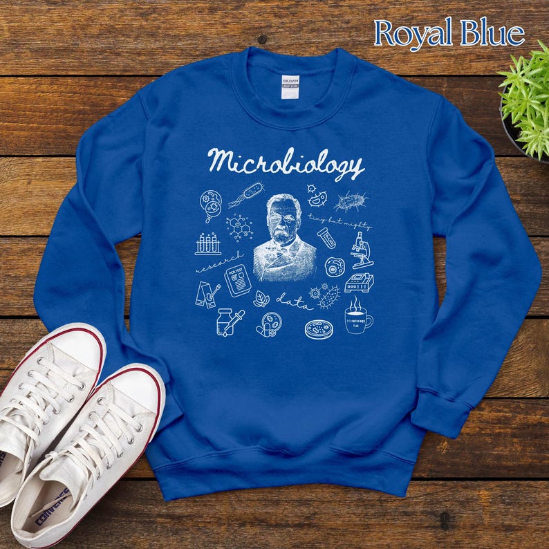 May include: Royal blue sweatshirt with the word "Microbiology" in white script. The design includes a portrait, scientific illustrations, and the words "research" and "data". White sneakers are visible in the lower left corner.