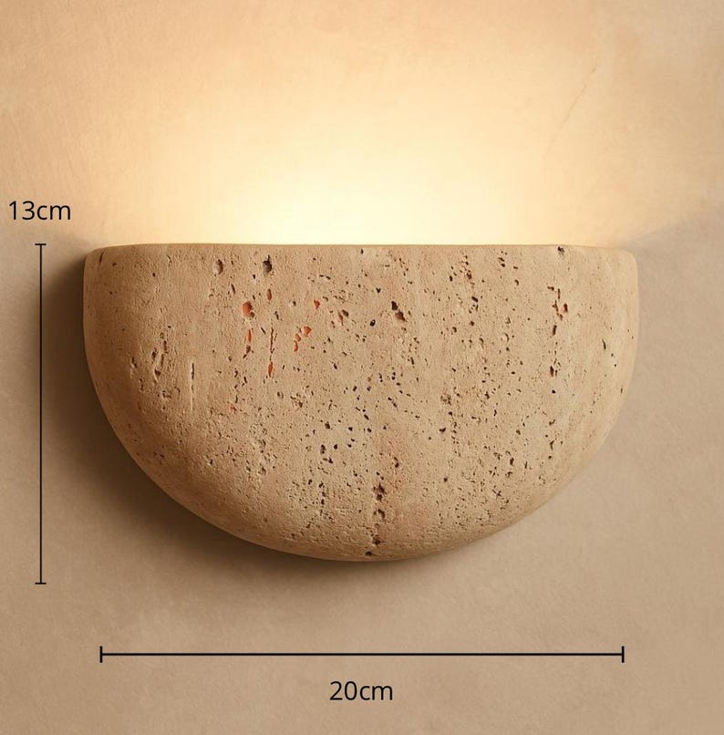 May include: A beige, semi-circular wall sconce made of textured stone. The sconce is 20 cm wide and 13 cm tall, with a warm light emanating from within. The design is minimalist and modern, suitable for interior lighting.