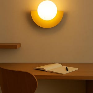 Può includere: Una moderna applique da parete minimalista con una sorgente luminosa sferica e luminosa inserita in una cornice gialla a forma di semicerchio. Sotto, una scrivania in legno con un taccuino aperto e una penna. La scena è illuminata dall'applique.