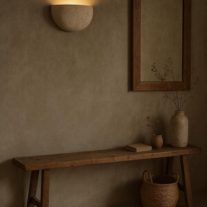 May include: A rustic interior scene featuring a wooden bench, a woven basket, and a decorative wall sconce. A framed mirror and vases with dried plants add to the natural aesthetic. The warm lighting creates a cozy atmosphere.