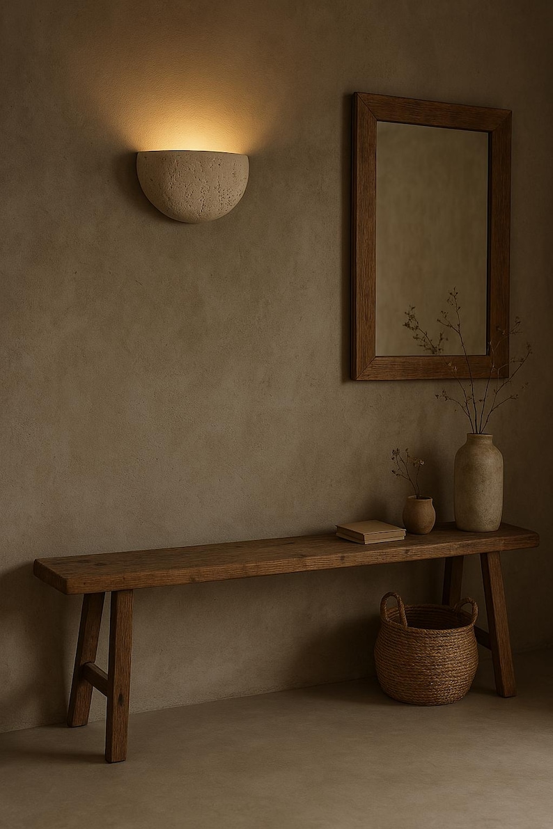May include: A rustic interior scene featuring a wooden bench, a woven basket, and a decorative wall sconce. A framed mirror and vases with dried plants add to the natural aesthetic. The warm lighting creates a cozy atmosphere.