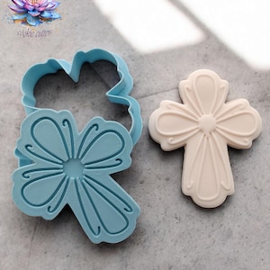 May include: A light blue cookie cutter in the shape of a flower and a beige cookie in the shape of a cross. The cookie cutter has a detailed design. The cookie is a light beige color. The logo "Dolcheria cookie cutters" is in the top left corner.