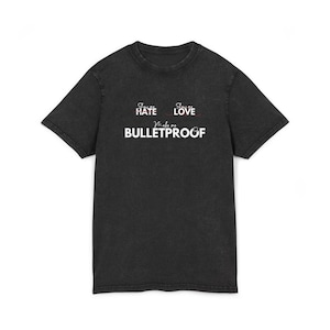 May include: Black t-shirt with the text "Show Hate, Show Love, Make me Bulletproof" in white and red lettering. The shirt has a crew neck and short sleeves. The fabric has a slightly faded, vintage look.