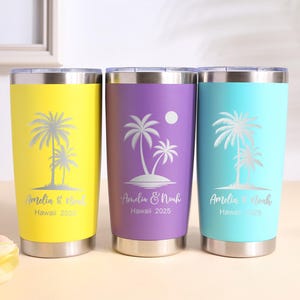 Puede incluir: Tres vasos de acero inoxidable en amarillo, morado y turquesa. Cada vaso presenta un diseño de palmera y el texto "Amelia & Noah Hawaii 2025". Los vasos tienen un borde y una base plateados.
