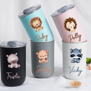 May include: A collection of insulated tumblers in various colors, each featuring a cute animal illustration and a name. The tumblers include a lion, hedgehog, bear, raccoon, and hippo. The names "Ruby", "Polly", "Sandy", "Vicky", and "Trista" are written on the tumblers.