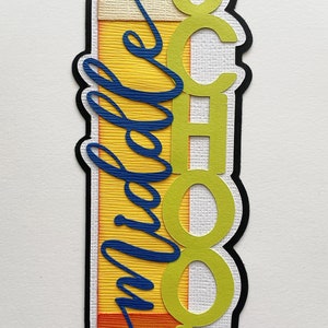 May include: A yellow, orange, and red pencil-shaped paper craft with the word "School" cut out in green letters. The word "middle" is written in blue cursive on the left side of the craft. The craft is 2.5 inches wide and 7 inches tall.