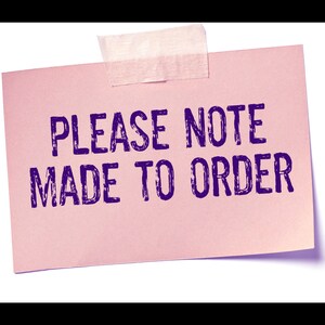 Puede incluir: Una nota rectangular de papel rosa claro sujeta con un trozo de cinta adhesiva transl&uacute;cida. La nota presenta el texto en color morado oscuro PLEASE NOTE MADE TO ORDER impreso en una fuente negrita sin remates en el centro del papel.