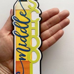 May include: A yellow pencil-shaped bookmark with the word "School" in green letters and the word "middle" in blue cursive writing.
