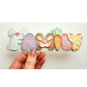 以下が含まれることがあります： 「FAMILY」と書かれた装飾的なサインで、各文字は異なるイースターをテーマにデザインされています。「F」は白いウサギ、「A」は足跡のある紫、「M」は茶色のウサギの顔、「I」はニンジン、「L」と「Y」はチーズです。