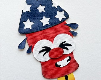 Op de afbeelding: Een grillig, patriottisch vuurwerkontwerp. Het vuurwerk heeft een rode behuizing met een blauwe en witte sterrenpatroon. Het heeft grote witte ogen, een rode neus en een lachende mond, met gele en oranje vlammen aan de onderkant.