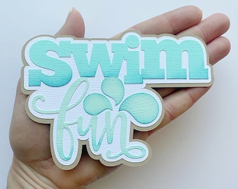 Może przedstawiać: Rękodzieło papierowe w kolorze turkusowym i białym z napisem "Swim Fun" w ozdobnym kroju pisma.