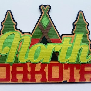 Puede incluir: Un recorte de papel en capas con el texto North Dakota en rojo y verde claro. El dise&ntilde;o incluye una forma de tipi central en verde y marr&oacute;n, flanqueada por dos pinos verdes, todo sobre un fondo azul oscuro con papel de textura marcada.