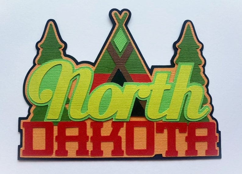 Puede incluir: Un recorte de papel en capas con el texto North Dakota en rojo y verde claro. El dise&ntilde;o incluye una forma de tipi central en verde y marr&oacute;n, flanqueada por dos pinos verdes, todo sobre un fondo azul oscuro con papel de textura marcada.
