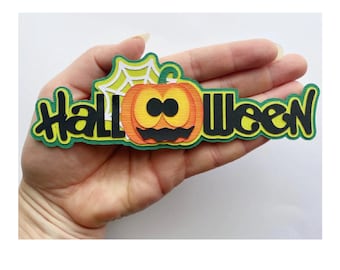 Może przedstawiać: Wielowarstwowa dekoracja na Halloween ze słowem "Halloween" w kolorze czarnym, obramowanym na zielono. Na dekoracji znajduje się również kreskówkowa dynia z uśmiechniętą twarzą i pajęczyną. Dekoracja jest trzymana w dłoni.