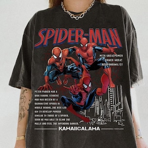 May include: Dark gray t-shirt featuring a graphic of Spider-Man in action poses. The design includes the text "SPIDER-MAN" in red and white, along with additional text describing the character's origin and the phrase "KAWAIICALAMA".