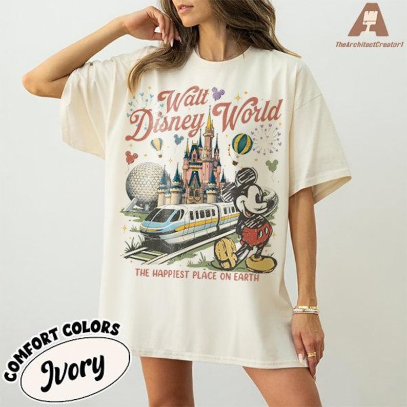 May include: Ivory-colored t-shirt featuring a vintage-style Walt Disney World graphic. The design includes a castle, train, Mickey Mouse, and the text "The Happiest Place on Earth." The shirt is from Comfort Colors.