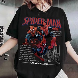 May include: Black t-shirt featuring three Spider-Man illustrations in red, blue, and black. The text "SPIDER-MAN" is in red and blue, with additional text describing the character's origin. The shirt also includes the text "KAWAIICALAMA".