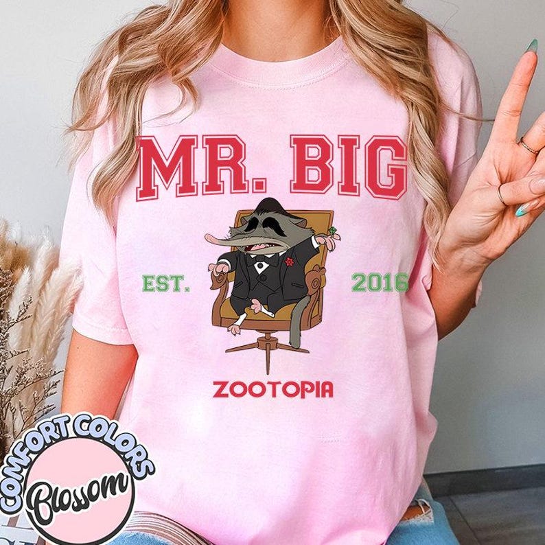 Puede incluir: Camiseta rosa claro con el texto "MR. BIG" en letras rojas. Debajo, una ilustraci&oacute;n de dibujos animados de una rata con traje, sentada en una silla. La camiseta tambi&eacute;n presenta el texto "EST. 2016" y "ZOOTOPIA".